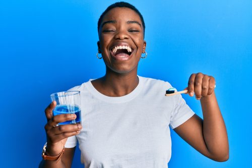 young woman in white shirt holds mouthwash and toothbrush